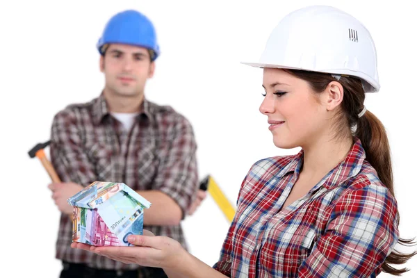 Kvinnliga och manliga byggnadsarbetare håller hus gjorda av pengar — Stockfoto
