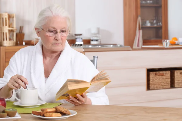 Пожилая женщина читает за завтраком — стоковое фото