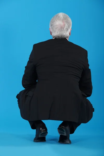 Senior businessman crouching with his back to the camera — Stock Photo, Image