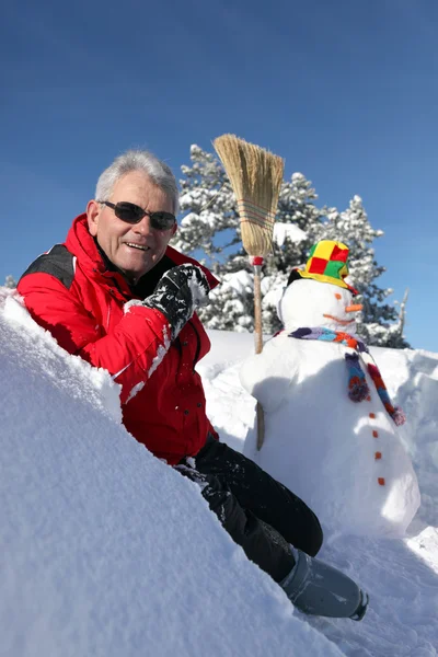 Чоловік сидів біля снігової людини — стокове фото