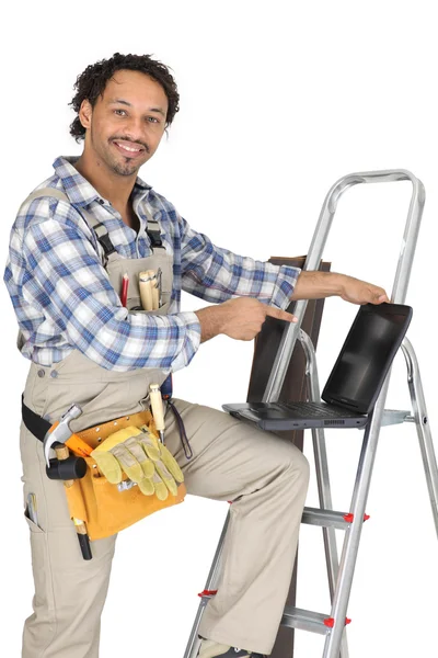 Handyman stood with ladder and pointing at laptop — Stock Photo, Image