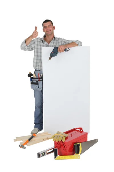 Aprovação comerciante posando com um sinal em branco e suas ferramentas — Fotografia de Stock