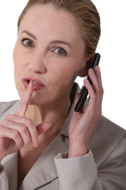 Woman indicating quiet whilst holding a phone clipart