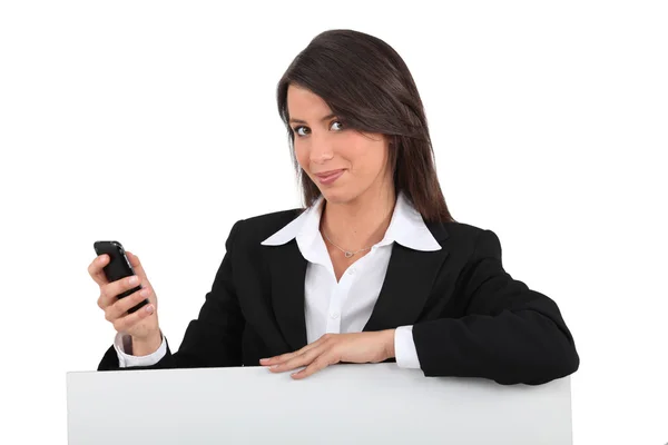 Businesswoman with mobile posing by blank poster — Stock Photo, Image