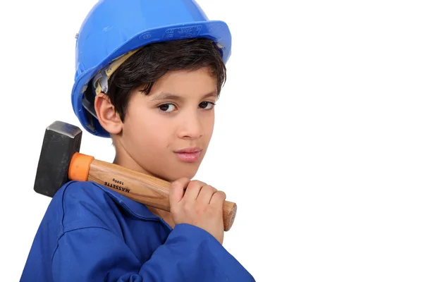 Liten pojke klädd som en hantverkare som håller en hammare — Stockfoto