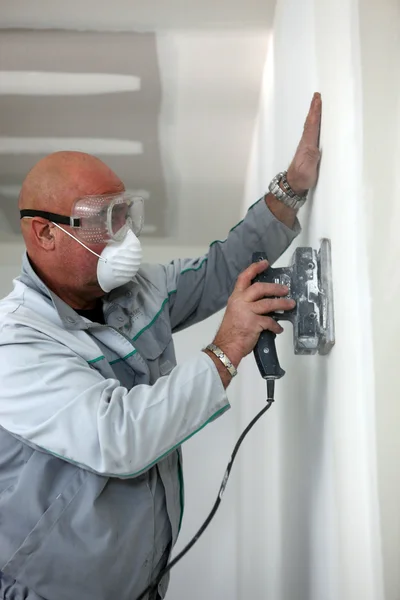 Uomo che indossa maschera e occhiali mentre carteggiatura parete — Foto Stock