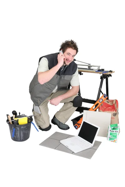 Craftsman making a call near laptop and miscellaneous tools — Stock Photo, Image