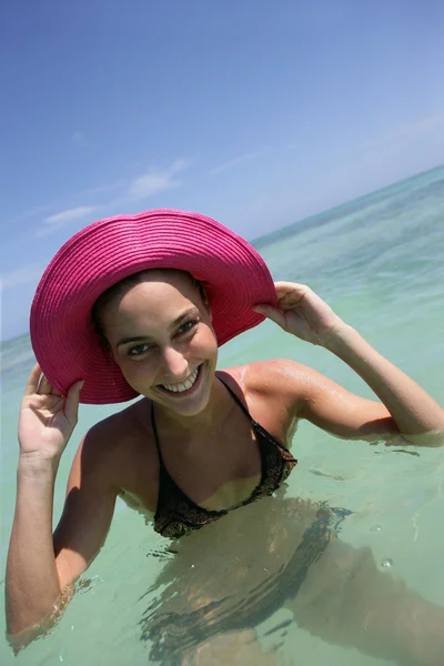 Transportando jovem mulher tomando banho com as mãos para seu chapéu de sol — Fotografia de Stock
