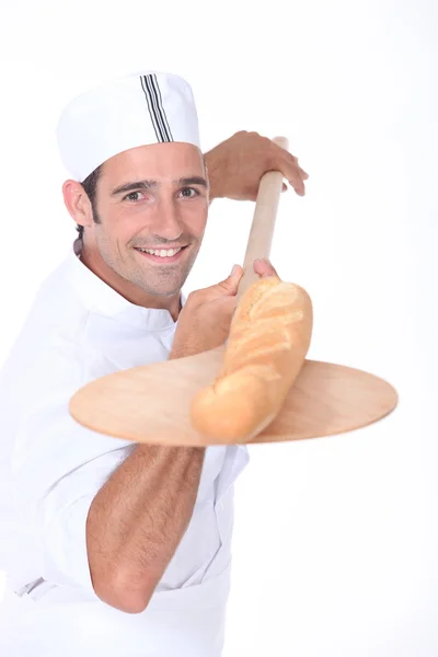 Baker pulling a freshly baked baguette out from the oven — Stock Photo, Image