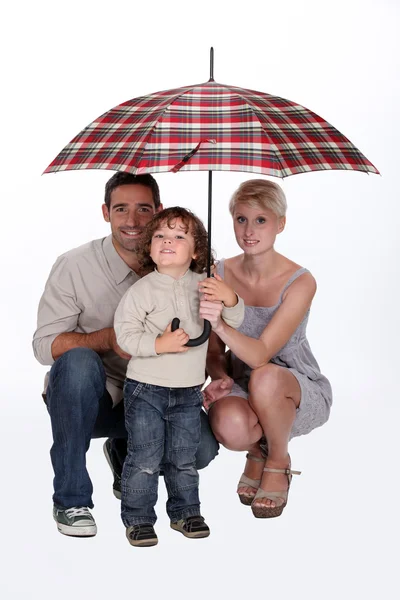 Young family sheltering under an umbrella — Stock Photo, Image