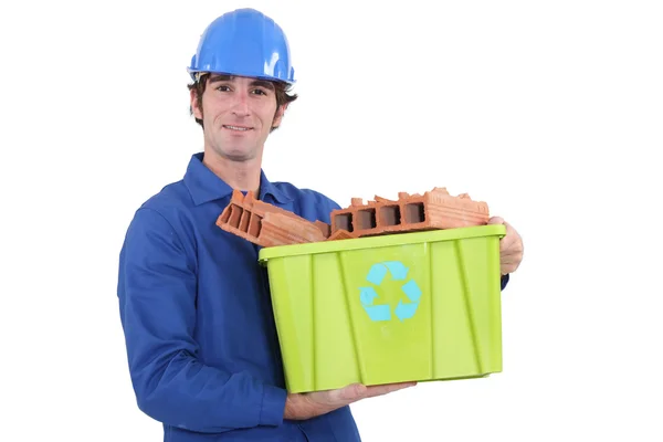Portrait of bricklayer in jumpsuit holding tub full of bricks with recycling logo — Stock Photo, Image