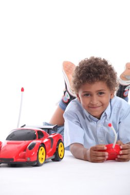 Young boy playing with a red remote control sports car clipart