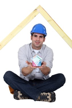 Carpenter sat cross-legged holding house made from bank notes clipart