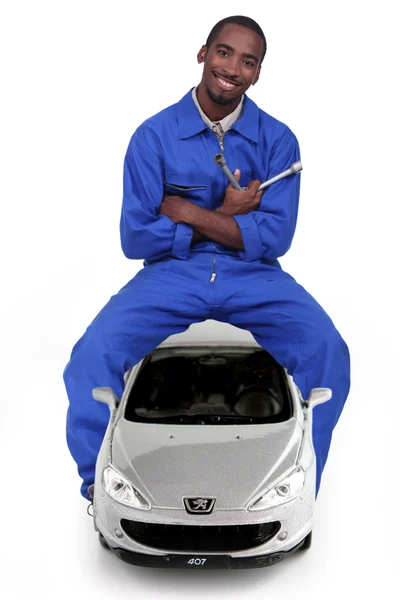 Mecánico sentado en un coche y sosteniendo una llave inglesa — Foto de Stock