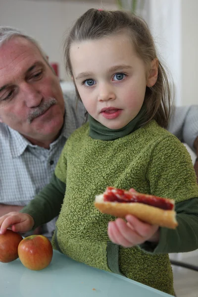 Bambina con nonno mangiare panino — Foto Stock