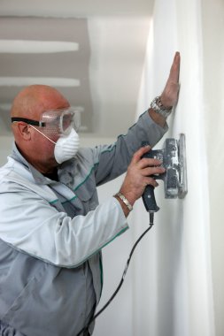 Man wearing mask and goggles whilst sanding wall clipart