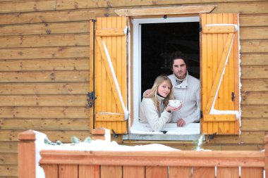 Couple looking out from chalet window clipart