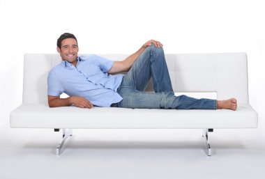 Barefoot man lying on a couch clipart