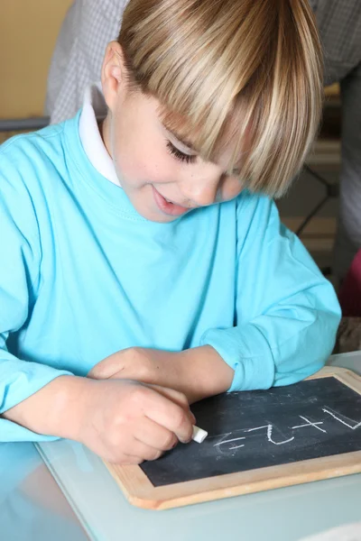 Kleiner Junge schreibt auf eine Schiefertafel — Stockfoto