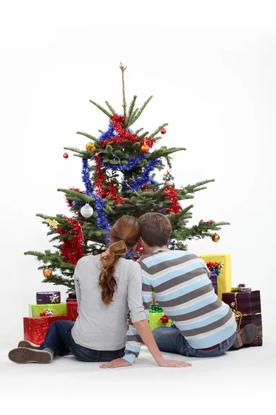 Casal sentado na frente de uma árvore de Natal — Fotografia de Stock