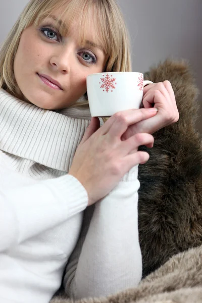 Женщина сидит на уютном диване с кружкой кофе — стоковое фото