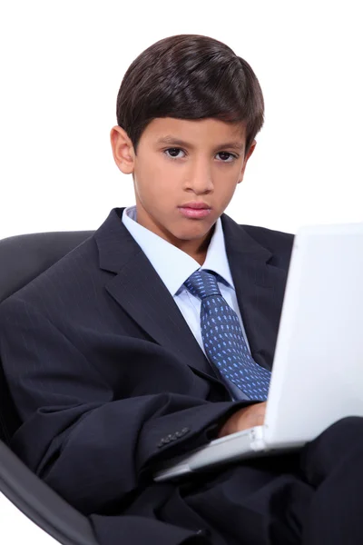 Serious young boy in an adult business suit with a laptop computer — Stock Photo, Image
