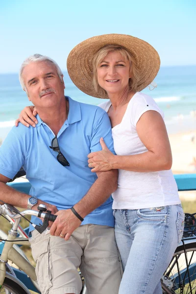 Középkorú pár élvezi a bike ride a tenger — Stock Fotó