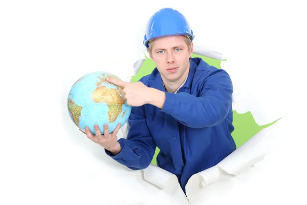 Een bouwvakker wijzend op een wereldbol. — Stockfoto