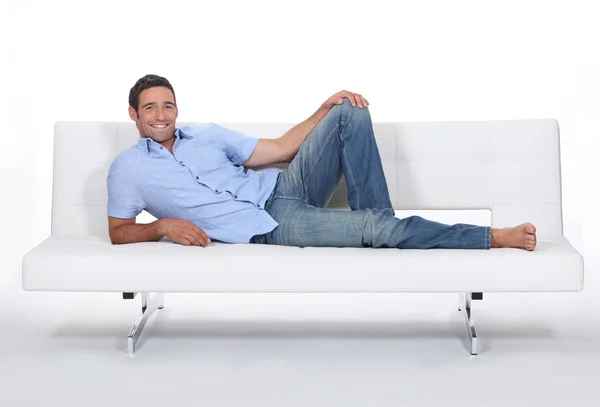 Barefoot man lying on a couch — Stock Fotó