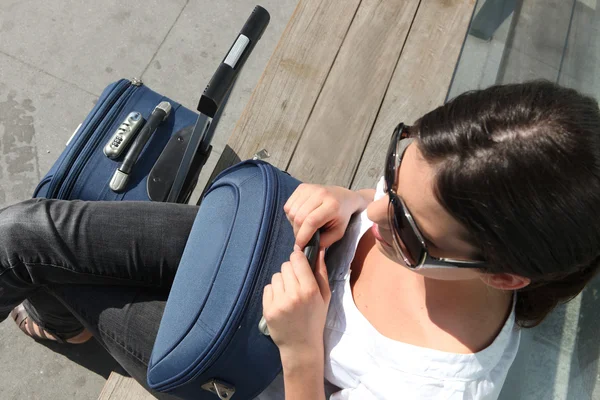 Žena s zavazadla sedí na lavičce — Stock fotografie