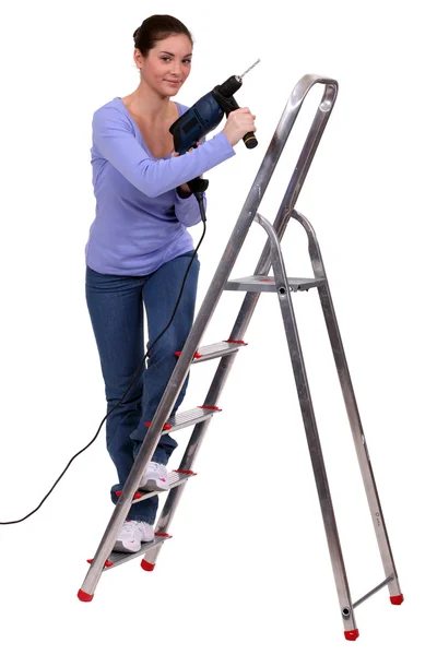 Vrouw op een trapladder met een powerdrill Stockfoto