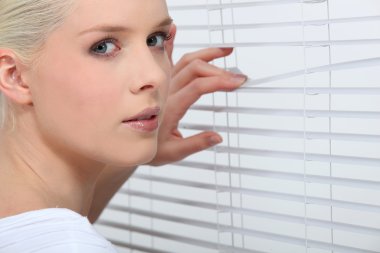 Nosy blond peering through window blinds clipart