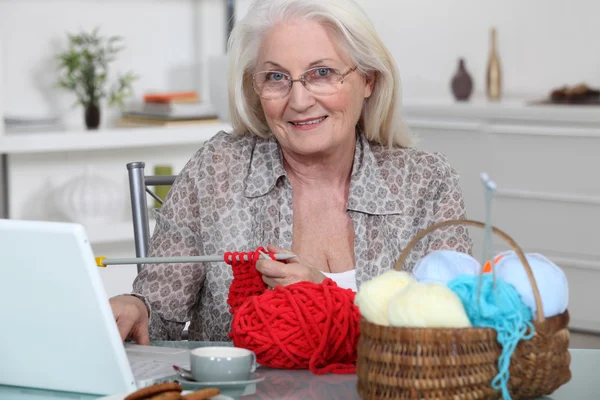 Senior woman knitting in front of her laptop computer — Stock Photo, Image
