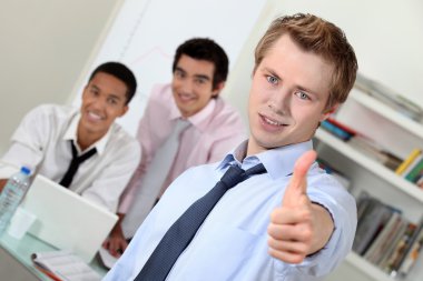 Young businessman giving thumbs-up during meeting clipart