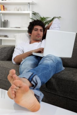 Man lying on sofa with computer clipart