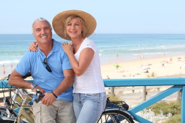 Mature couple with bikes by the beach clipart