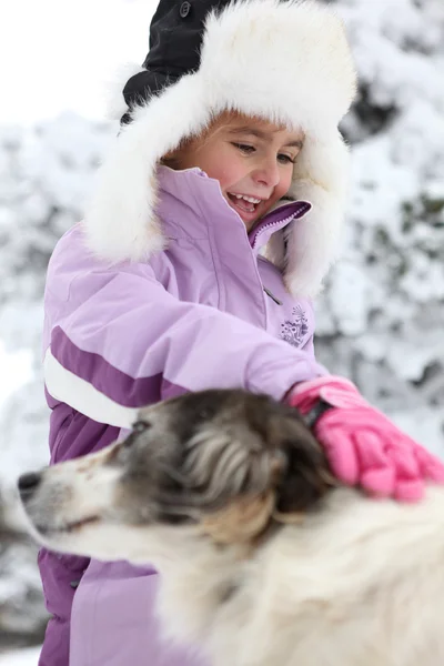 Little girl petting dog in the snow — Stock Photo, Image