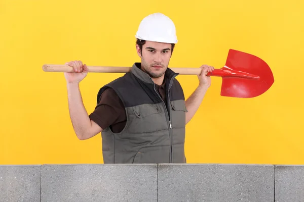 Кирпич держит лопату возле бетонной стены — стоковое фото