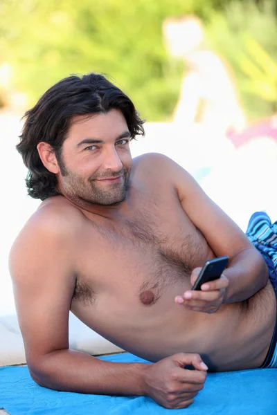 Mann im Badeanzug schaut auf sein Handy — Stockfoto