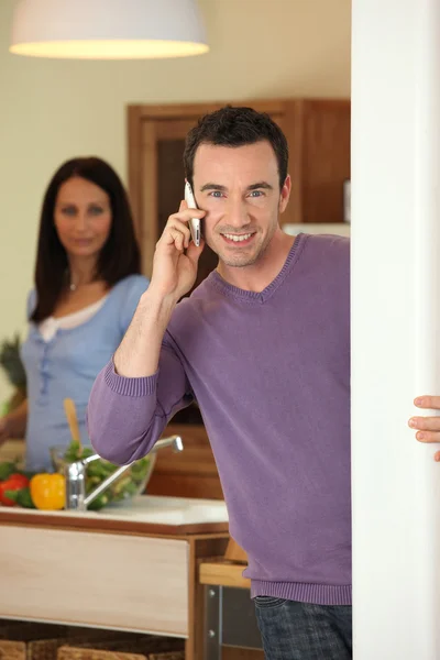 Man making a call whilst wife prepares meal — Stock Photo, Image