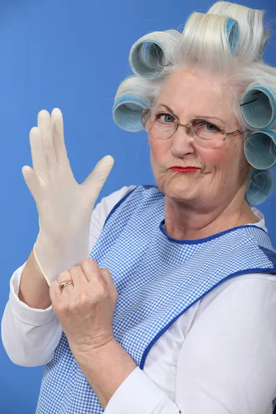 Granny with her hair in rollers putting on a latex glove — Stock Photo, Image