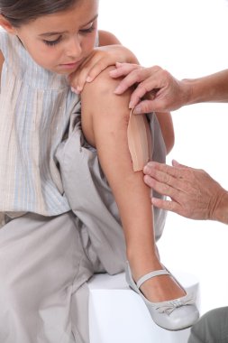 Woman putting band-aid on little girl's leg clipart