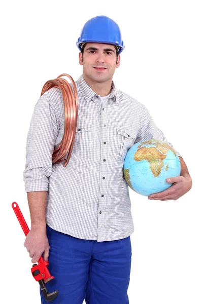 Handelaar holding een wereldbol, een opgerolde koperdraad en een pipe wrench — Stockfoto