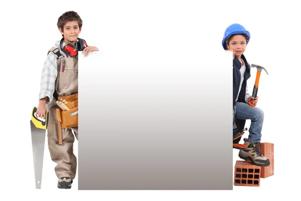 Bambini che fingono di essere operai edili in piedi intorno a un cartello vuoto — Foto Stock