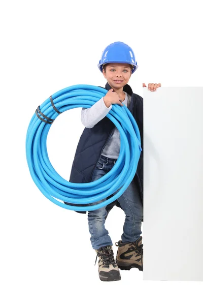 Ung pojke klädd som en rörmokare med en styrelse tomt för ditt meddelande — Stockfoto