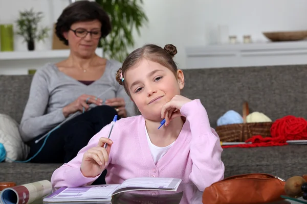 Kleines Mädchen macht ihre Hausaufgaben, während ihre Mutter näht — Stockfoto