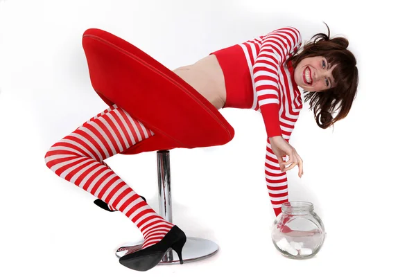 Fiatal nő, piros-fehér csíkos ruhát megpróbálja elérni a jar tele bonbon — Stock Fotó