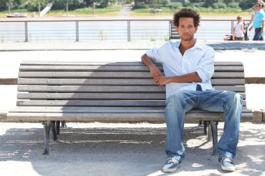 Young man sitting on a public bench clipart