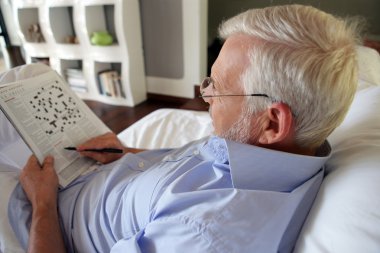 Grey-haired man completing crossword puzzle clipart