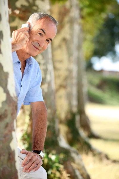 Человек с телефоном за деревом — стоковое фото